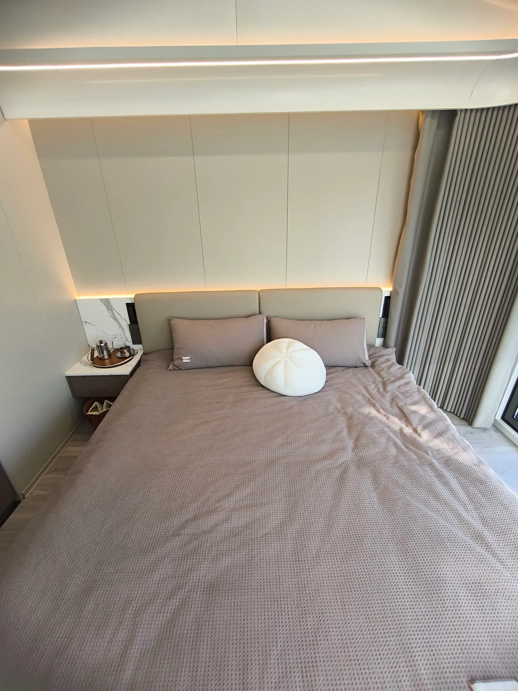 Schlafbereich einer Wohnzelle mit Doppelbett, Einbauschränken und indirekter Beleuchtung