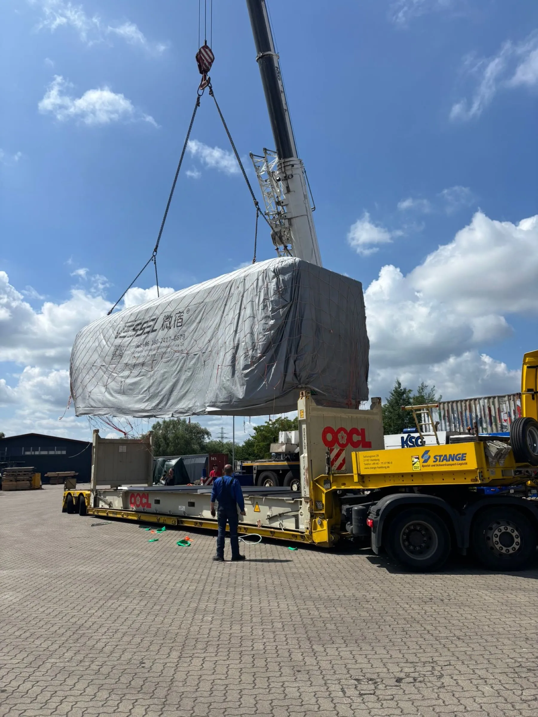 Verpackte Wohnzelle wird am Depot per Kran auf den Spezialauflieger gesetzt